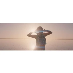 Backlit figure of a woman wearing a sequined top standing in shallow water against a bright setting sun with anamorphic lens flare.