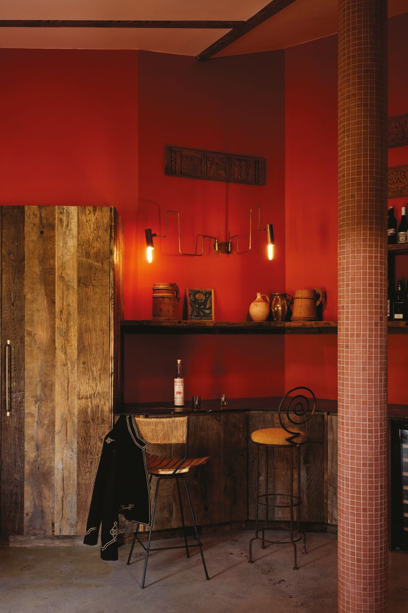Rustic interior featuring wooden wall paneling, vintage chairs, and a small bar area with bottles and warm lighting. The room is red.