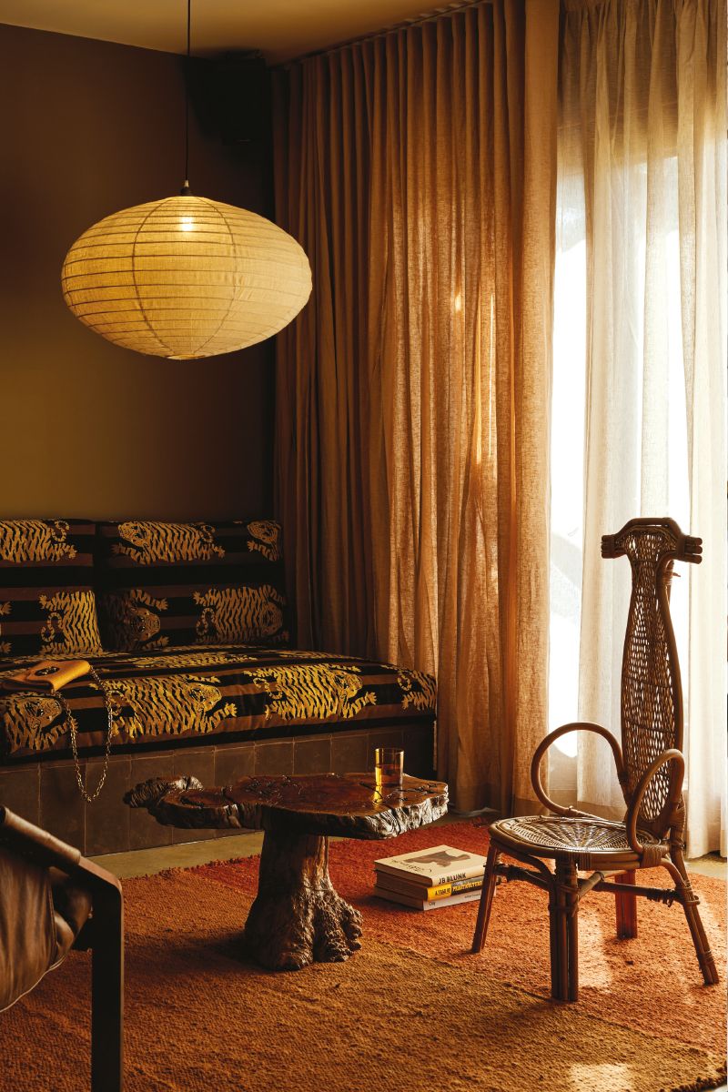Cozy living room interior with natural light, featuring a hanging paper lamp, daybed, unique table, rattan chair, and earthy tones.