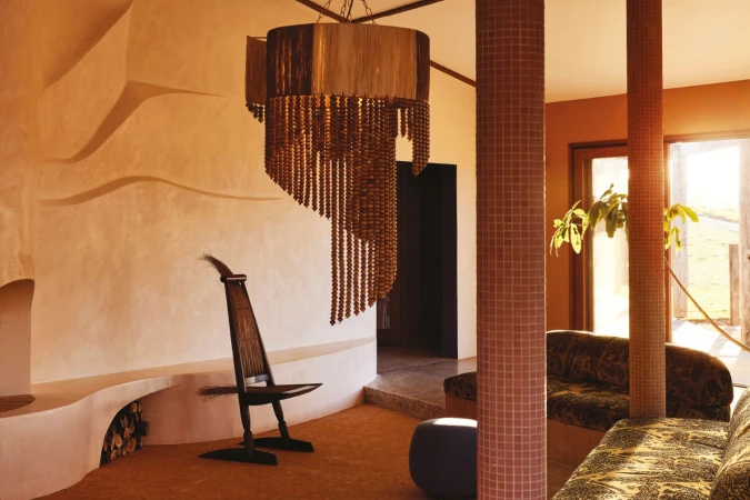 Interior view of a home showcasing a unique chandelier, custom fireplace, and a distinctive chair with decorative accents in warm lighting.