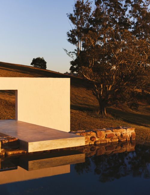 Minimalist architecture featuring a modern building facade and reflecting pool, set against a backdrop of rolling hills and trees.