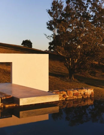 Minimalist architecture featuring a modern building facade and reflecting pool, set against a backdrop of rolling hills and trees.