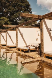 Outdoor pool area with wooden daybeds under timber pergolas and stone paving for InStyle Australia Ranch Life