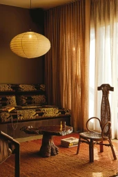 Interior shot of a living room with a paper lantern pendant light, wooden stump coffee table, woven chair, and patterned sofa.