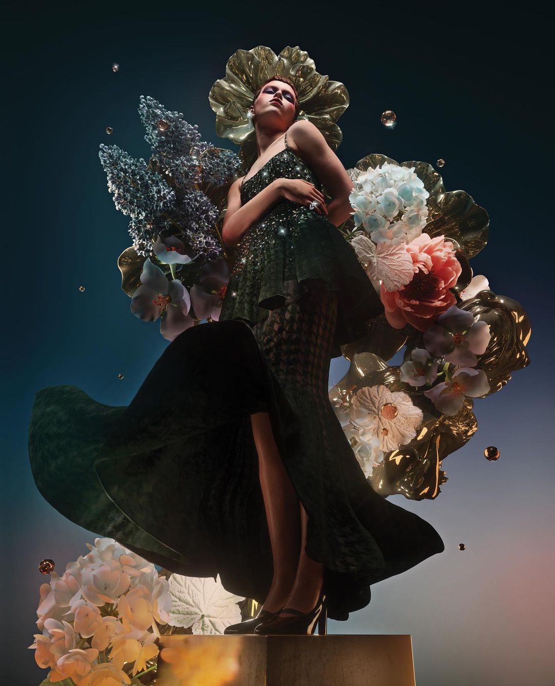 Woman in a green dress poses amidst an arrangement of artificial flowers, elevated on a gold base against a dark blue backdrop.