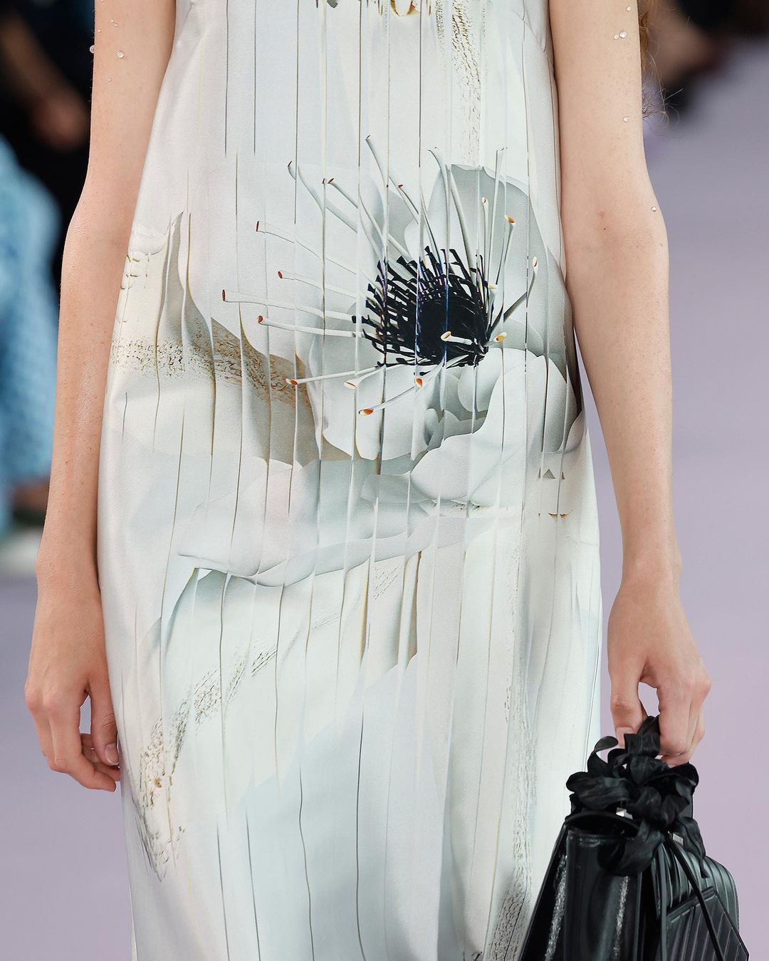 Close-up of a woman wearing a white dress with a large floral print and carrying a black purse, fashion, style.