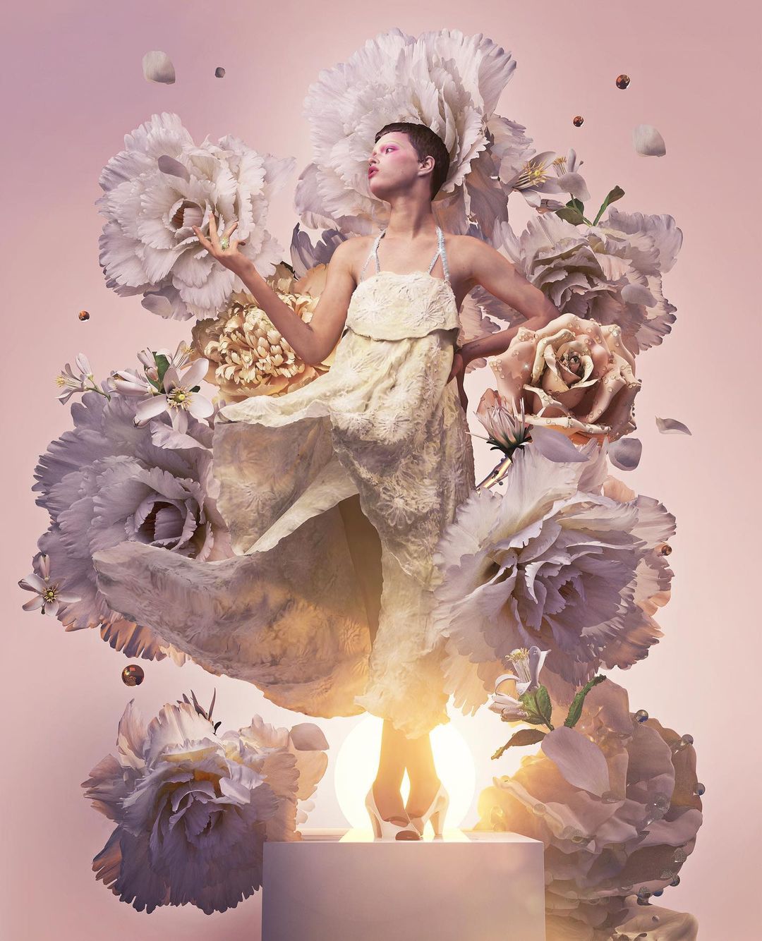 Woman in a white dress surrounded by large white and peach flowers, standing on a podium with glowing light, on a pink background.