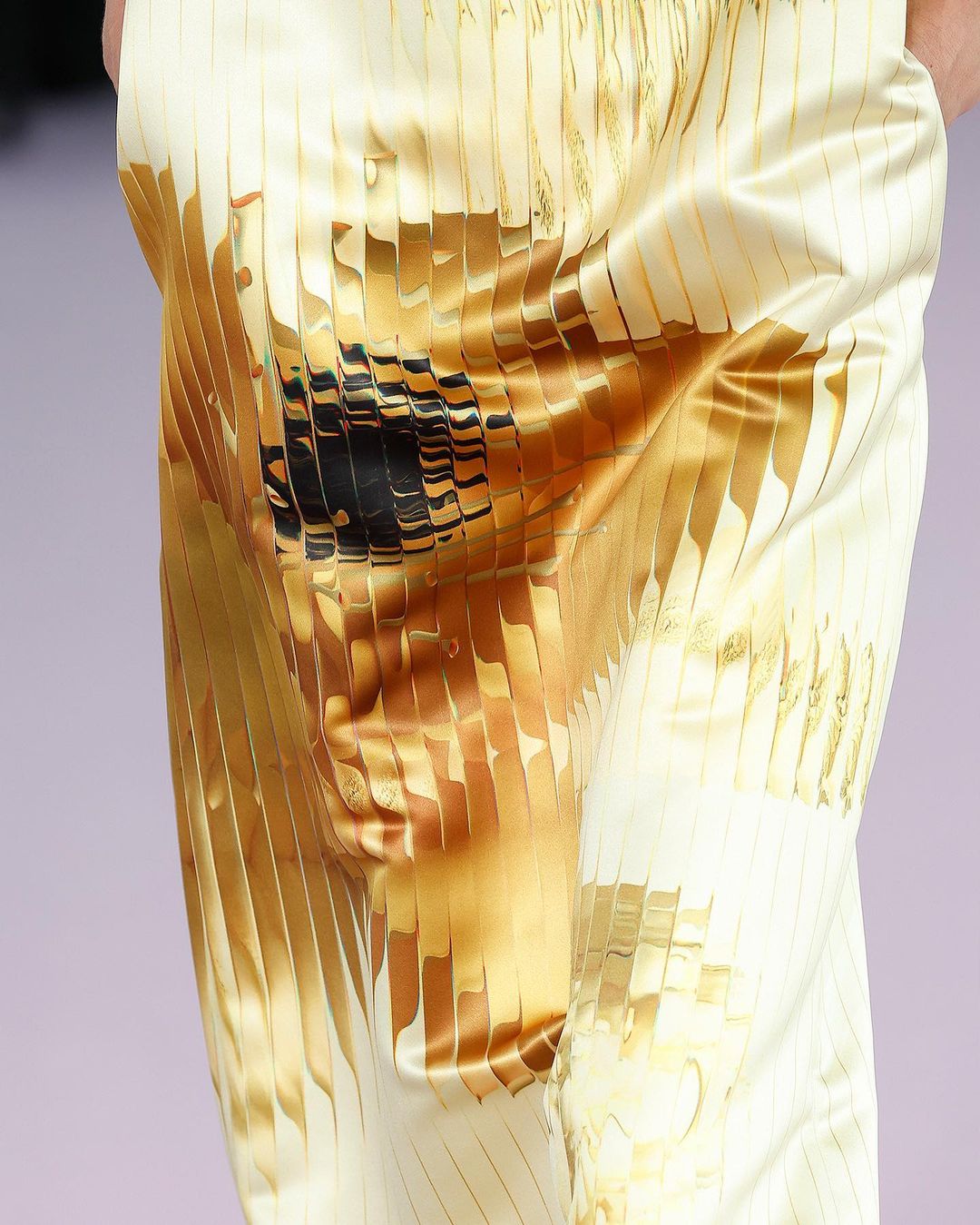 Close-up of shiny gold and white patterned fabric draped with draped folds, suggesting movement and abstract design elements.