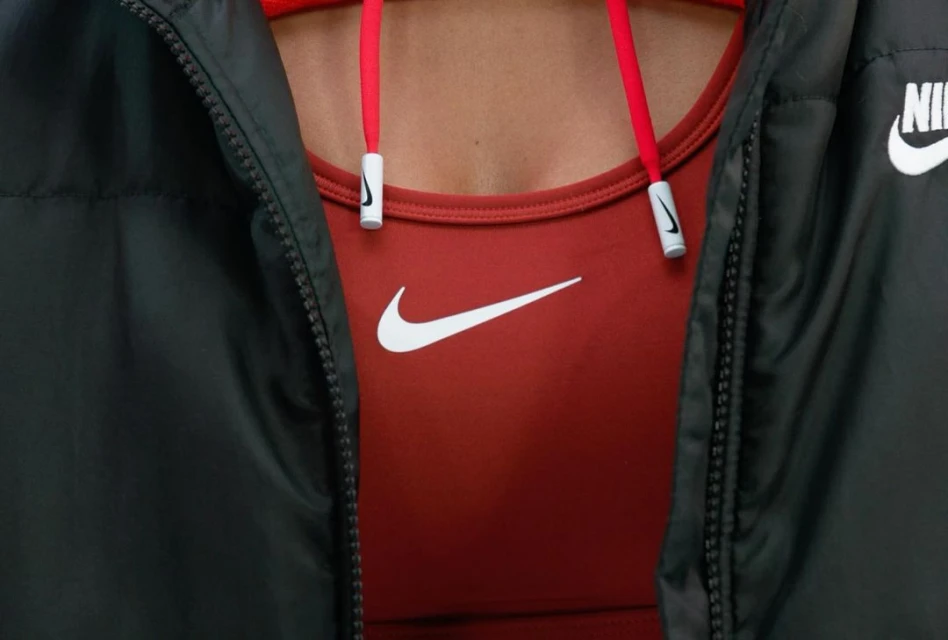 Close-up of a person wearing a rust-colored Nike sports bra with a white swoosh logo, paired with a black Nike jacket, showing the logo.
