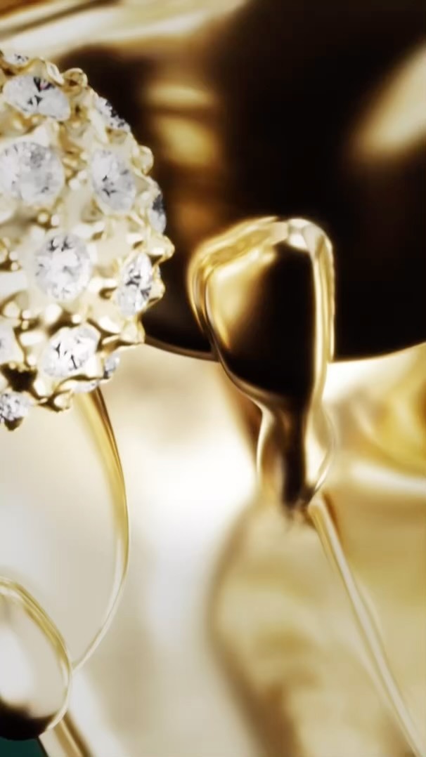 Close-up of abstract, reflective gold surfaces with white beaded floral accent on a dark background, showcasing luxurious shine and form.