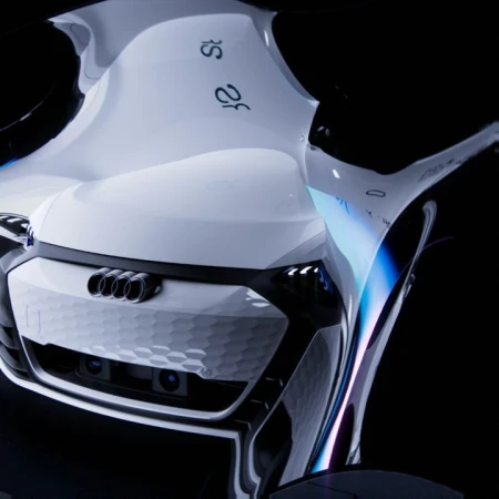Futuristic white Audi concept car with sleek lines and a hexagonal grille design against a dark background, highlighting automotive innovation.