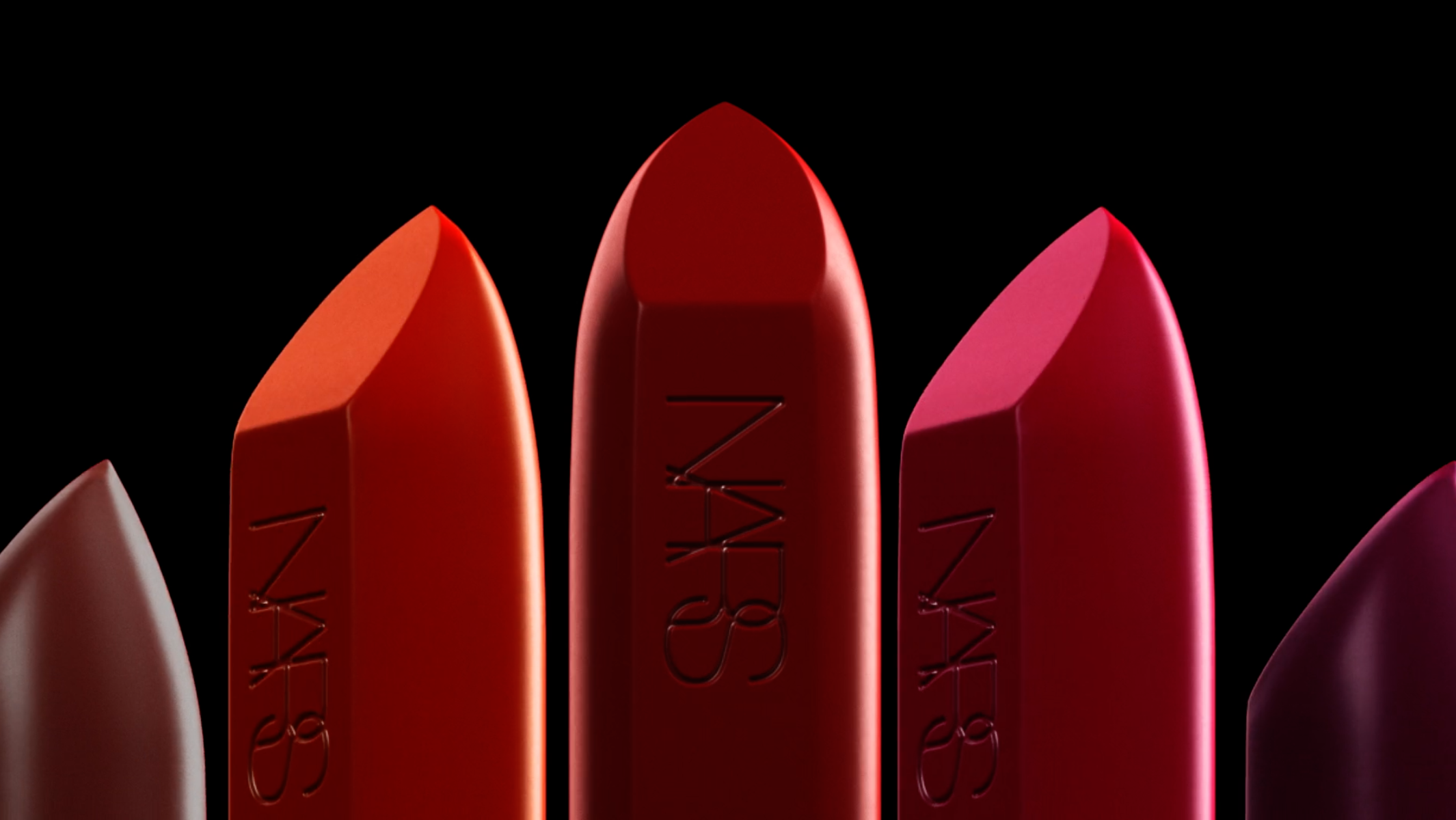 Close-up of NARS lipsticks in red, orange, and pink hues against a stark black backdrop, emphasizing the brand's cosmetic elegance.