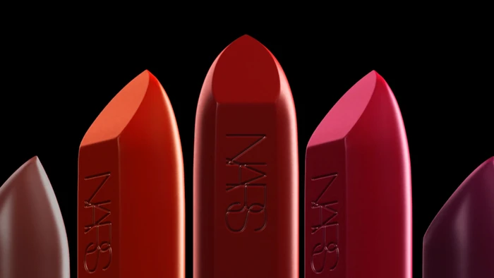 Close up of five upright red and berry lipstick bullets with embossed branding against a dark background
