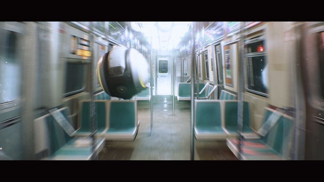 Empty subway car with green seats and metal poles, illuminated by bright white light, suggesting a still from a futuristic transport scene.