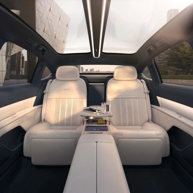 Car interior featuring white leather seats, a panoramic sunroof, and a modern design with a city building visible in the background.