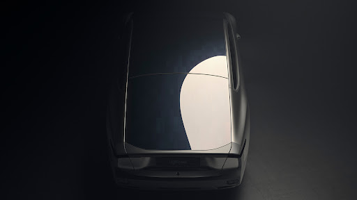 Overhead shot of a silver car with a rounded shape and a dark blue roof, set against a dark background in a photo studio.