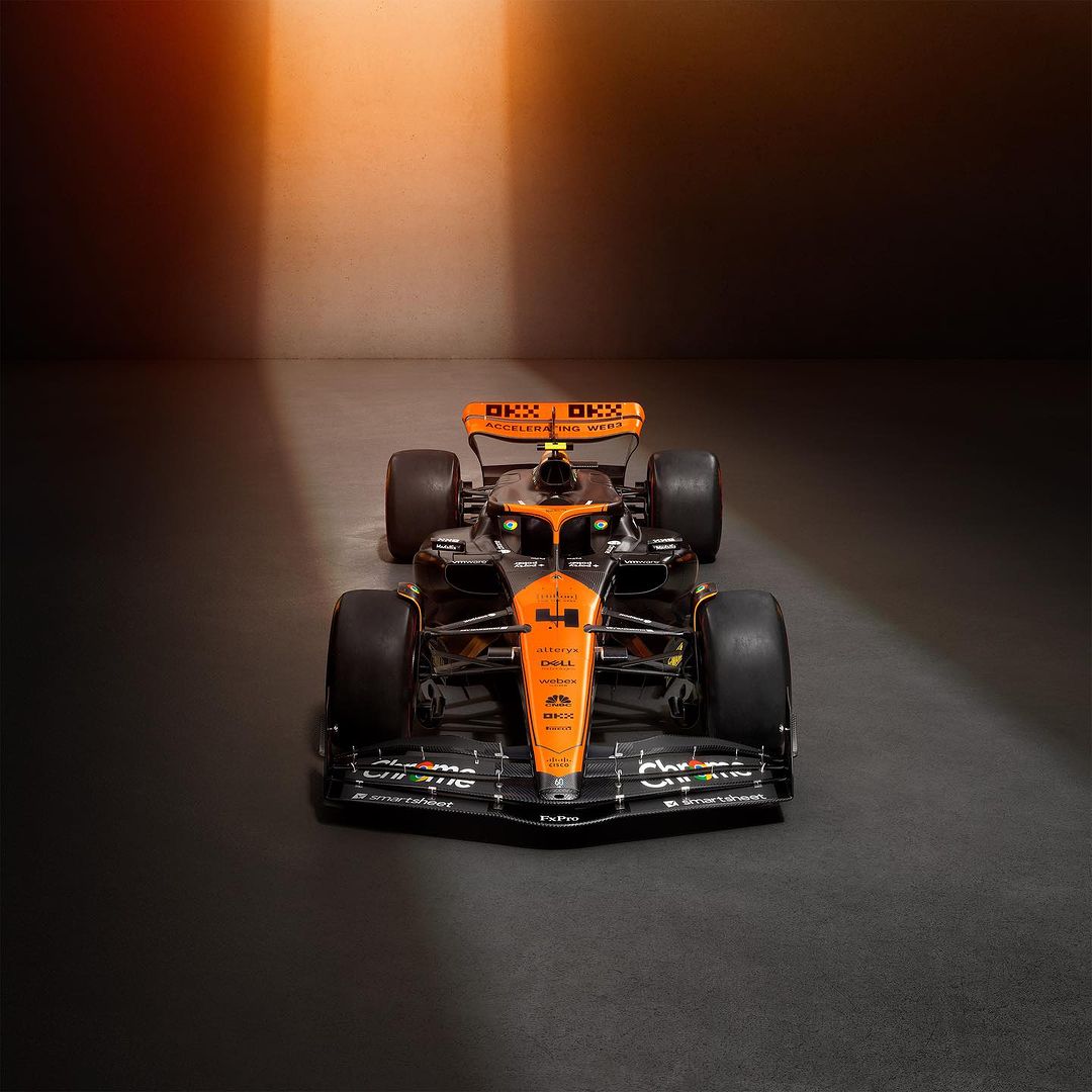 McLaren Formula 1 race car, a sleek vehicle with orange and black livery, positioned in a spotlight against a gradient dark background.