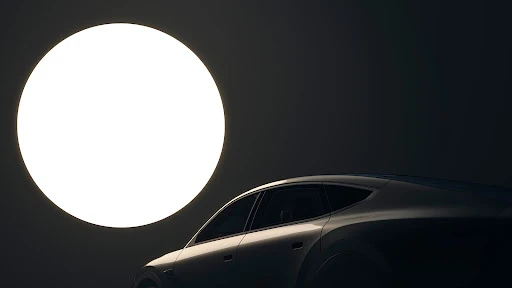 Sleek silver car in studio lighting with a large, bright circular light source in the background, creating a modern, automotive scene.