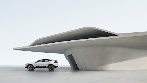 Sleek white electric SUV parked beside a modern concrete building near the ocean on a bright day. Automotive design with architectural backdrop.