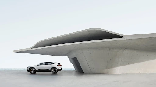 Sleek white electric SUV parked beside a modern concrete building near the ocean on a bright day. Automotive design with architectural backdrop.