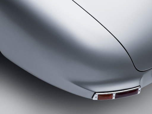 Rear fender detail of a silver vintage car with chrome trim and a two-tone amber and red tail light against a gray gradient background.