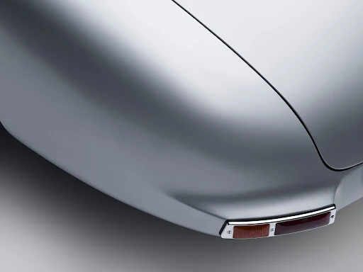 Rear fender detail of a silver vintage car with chrome trim and a two-tone amber and red tail light against a gray gradient background.