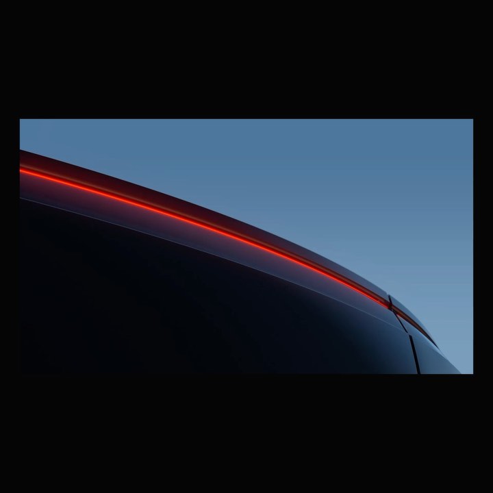 Close-up of the rear lights and top part of a dark blue automobile against a light blue sky, showcasing its sleek design.