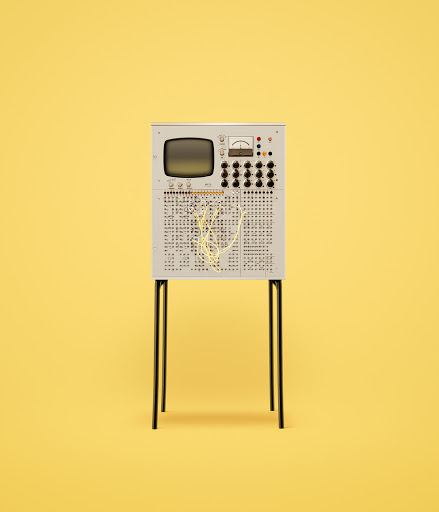Vintage computer with monitor and button panel on a yellow background. The computer has a boxy design with wires and a small screen.