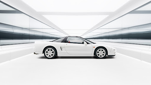 Side view of a white Honda NSX sports car parked inside a modern, minimalist garage featuring glossy white walls and floor.