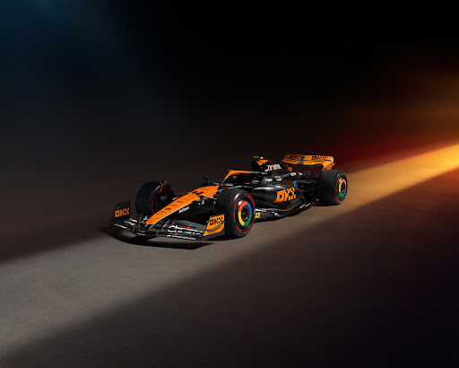 Sleek McLaren Formula 1 race car on display with striking orange and black livery, showcasing aerodynamic design against dark backdrop.