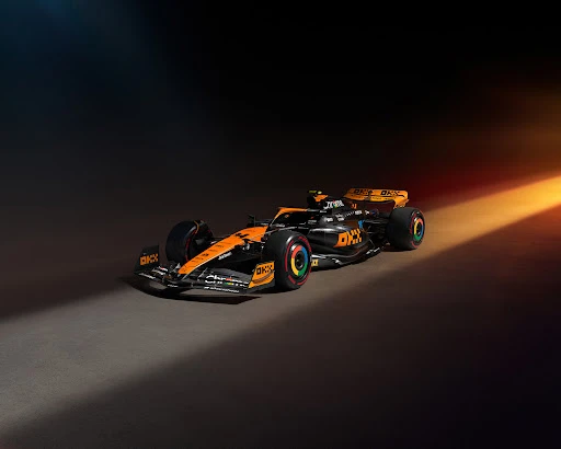 Sleek McLaren Formula 1 race car on display with striking orange and black livery, showcasing aerodynamic design against dark backdrop.