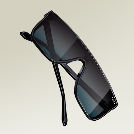 Close-up of black rectangular sunglasses with dark lenses on a beige background, featuring the brand logo on the lens.