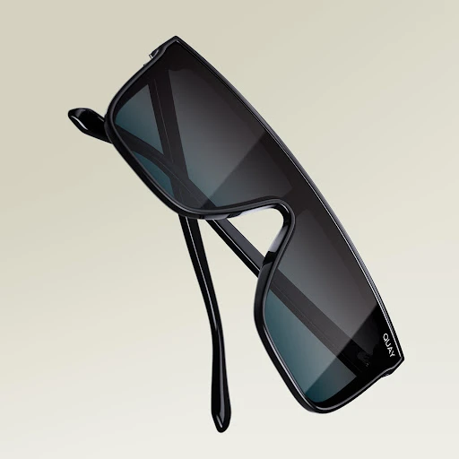 Close-up of black rectangular sunglasses with dark lenses on a beige background, featuring the brand logo on the lens.