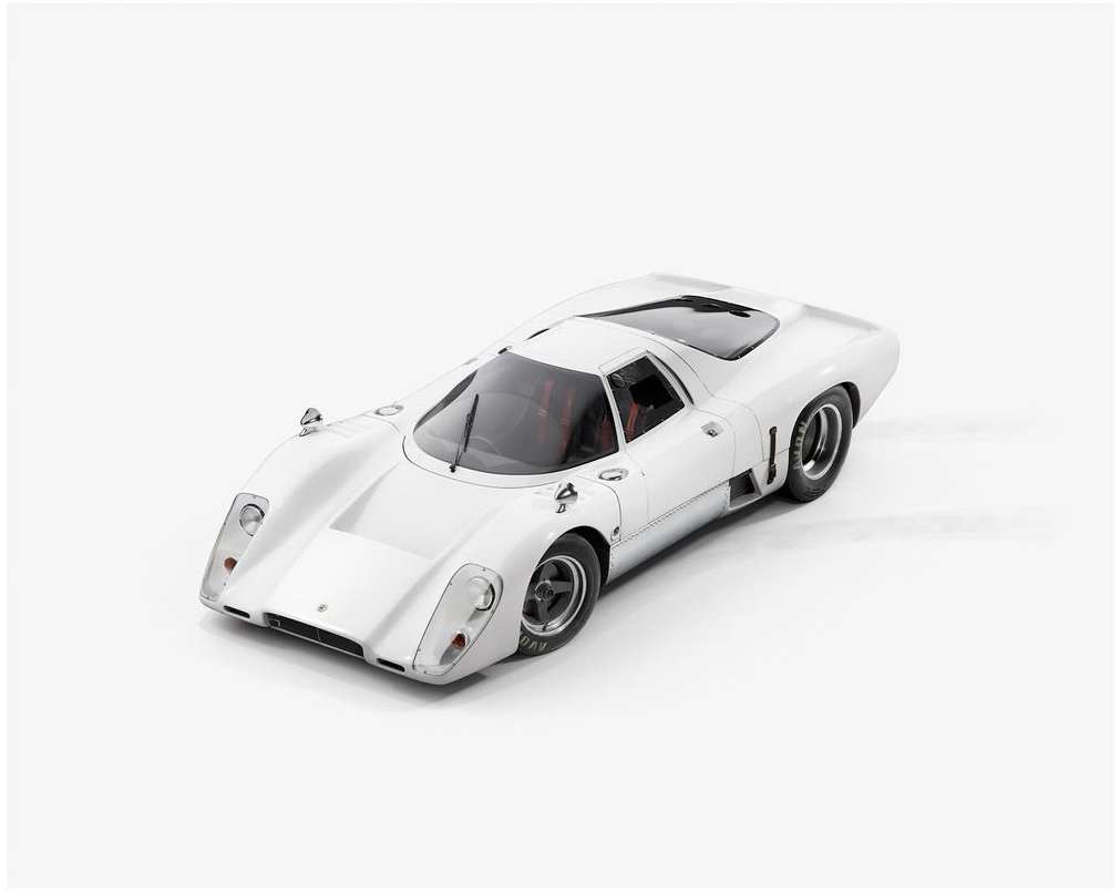 White race car parked in a photo studio setting, highlighting its sleek design, low profile, and vintage racing aesthetic.