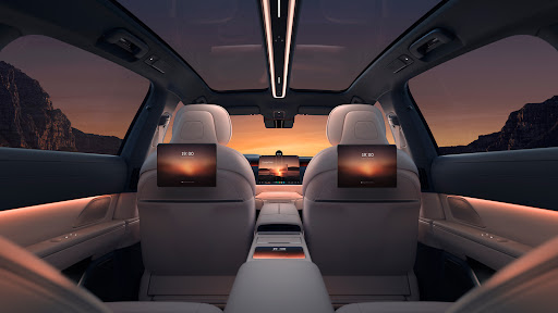 Beige leather interior of a luxury car with digital displays on headrests and dashboard; scenic mountain landscape outside the windows.