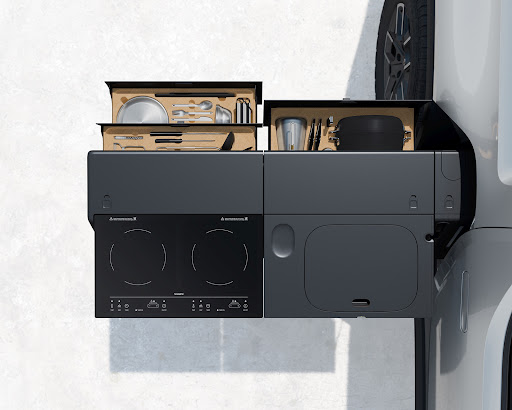 Minimalist RV kitchen module featuring a two-burner induction cooktop, sink, cutlery, and dishware against a neutral background, showcasing compact design.