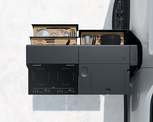Minimalist RV kitchen module featuring a two-burner induction cooktop, sink, cutlery, and dishware against a neutral background, showcasing compact design.