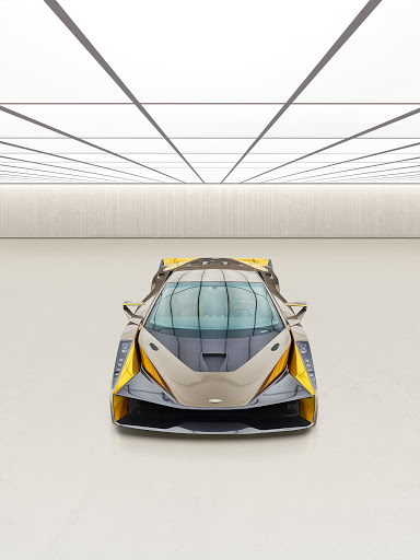 Frontal view of a grey and yellow sports car with a sleek design in an indoor auto studio with a glossy white floor and ceiling.