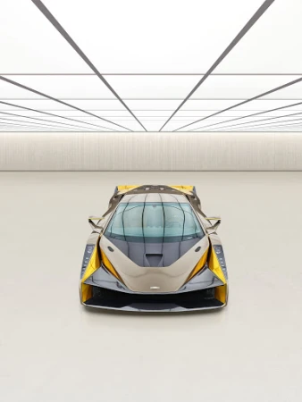 Frontal view of a grey and yellow sports car with a sleek design in an indoor auto studio with a glossy white floor and ceiling.