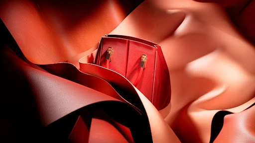 Red leather purse sits amidst flowing swathes of red and peach leather, highlighted by dramatic lighting that accents the material's texture.