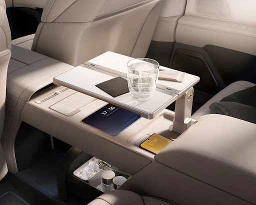 Car interior with a luxury table, complete with a glass of water, tablet, and phone, offering a comfortable workspace on the go.