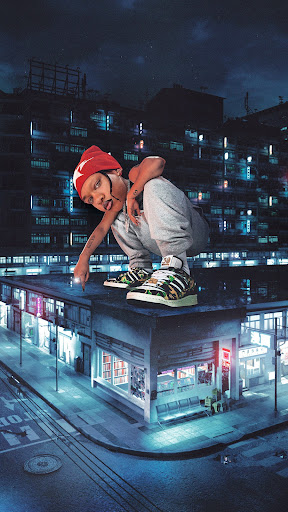 A person in a red hat poses on a building rooftop at night, wearing sneakers and a tracksuit, with the city lights in the background.