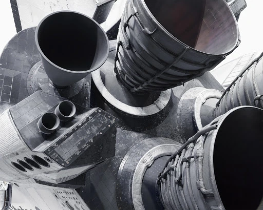 Monochromatic image of the Space Shuttle's rear, featuring multiple large nozzles and intricate mechanical details against a plain background.