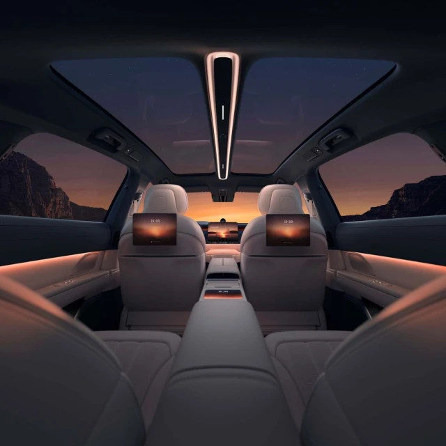 Car interior view with screens on back of seats showing sunset; the moon is visible through the sunroof and back window at dusk.