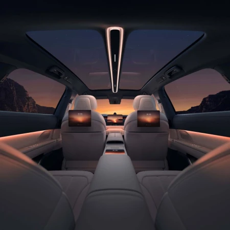 Car interior view with screens on back of seats showing sunset; the moon is visible through the sunroof and back window at dusk.