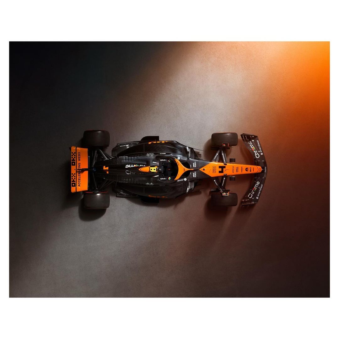 Overhead shot of a black and orange Formula 1 race car, angled, showcasing its aerodynamic design and glossy finish against a dark background.