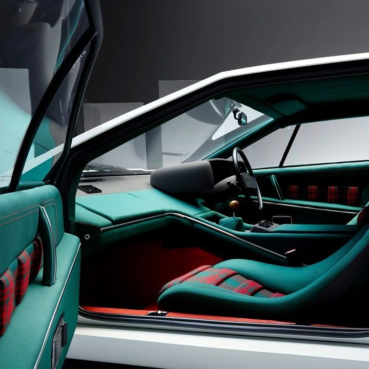 Interior view of a white vintage car with teal trim and red-and-green plaid seats, featuring an open door and a focus on the driver's side.