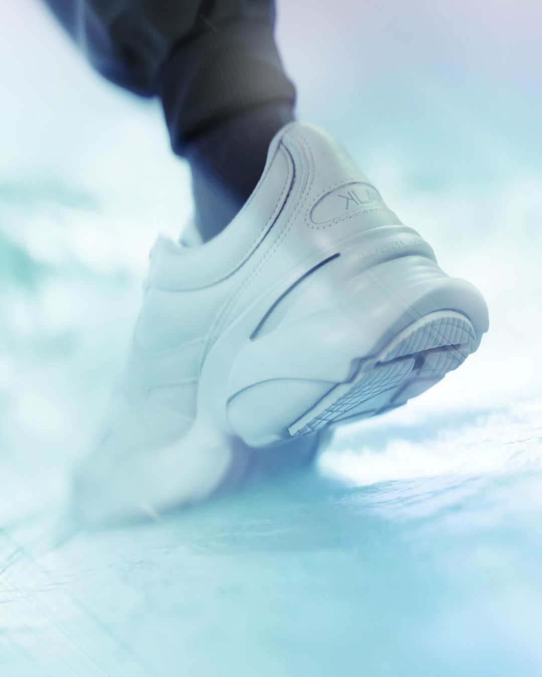Close-up of a white running shoe with a dark ankle sock, set against a blurred blue background, focused on sport and fitness.