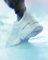 Close-up of a chunky white sneaker on a person's foot against a light blue icy textured background