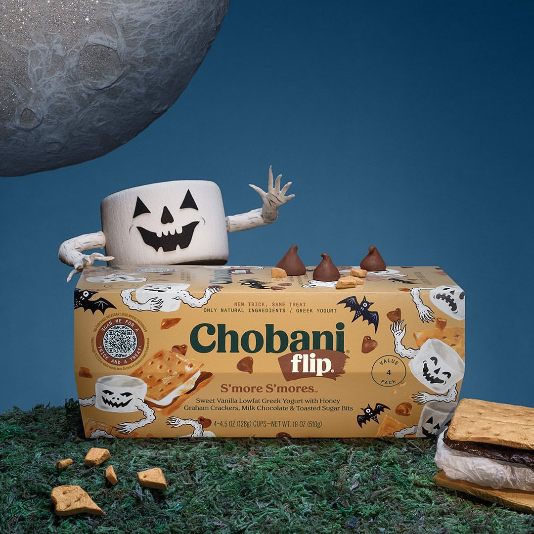 Chobani S'more S'mores yogurt carton with Halloween marshmallow character and graham cracker, chocolate treat, blue backdrop.